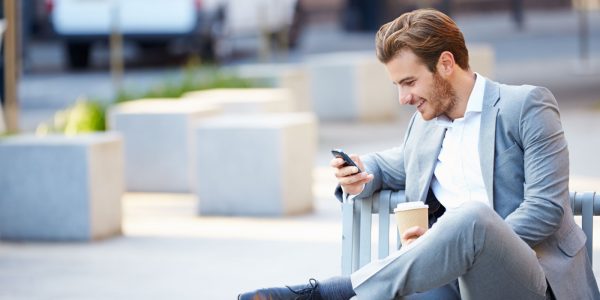 Мужчина с кофе и телефоном сидит на улице